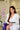 Woman in a white dress sitting on a purple couch with a pink flower in the background